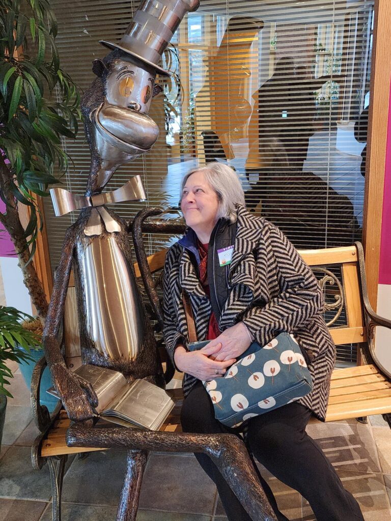 A woman sits on a bench next to a big metal Cat in the Hat