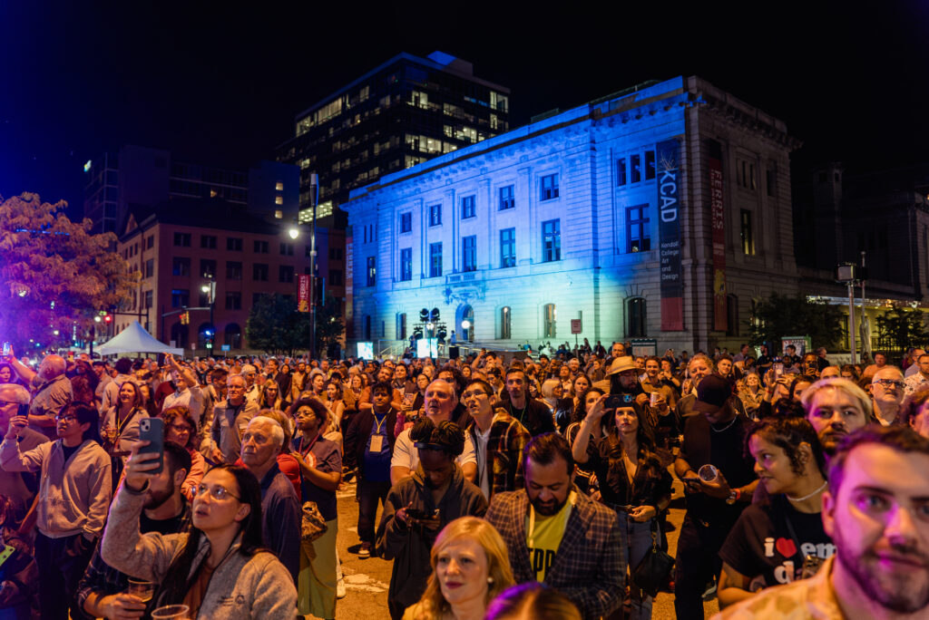 A crowd of people at night in front of a lit-up building.