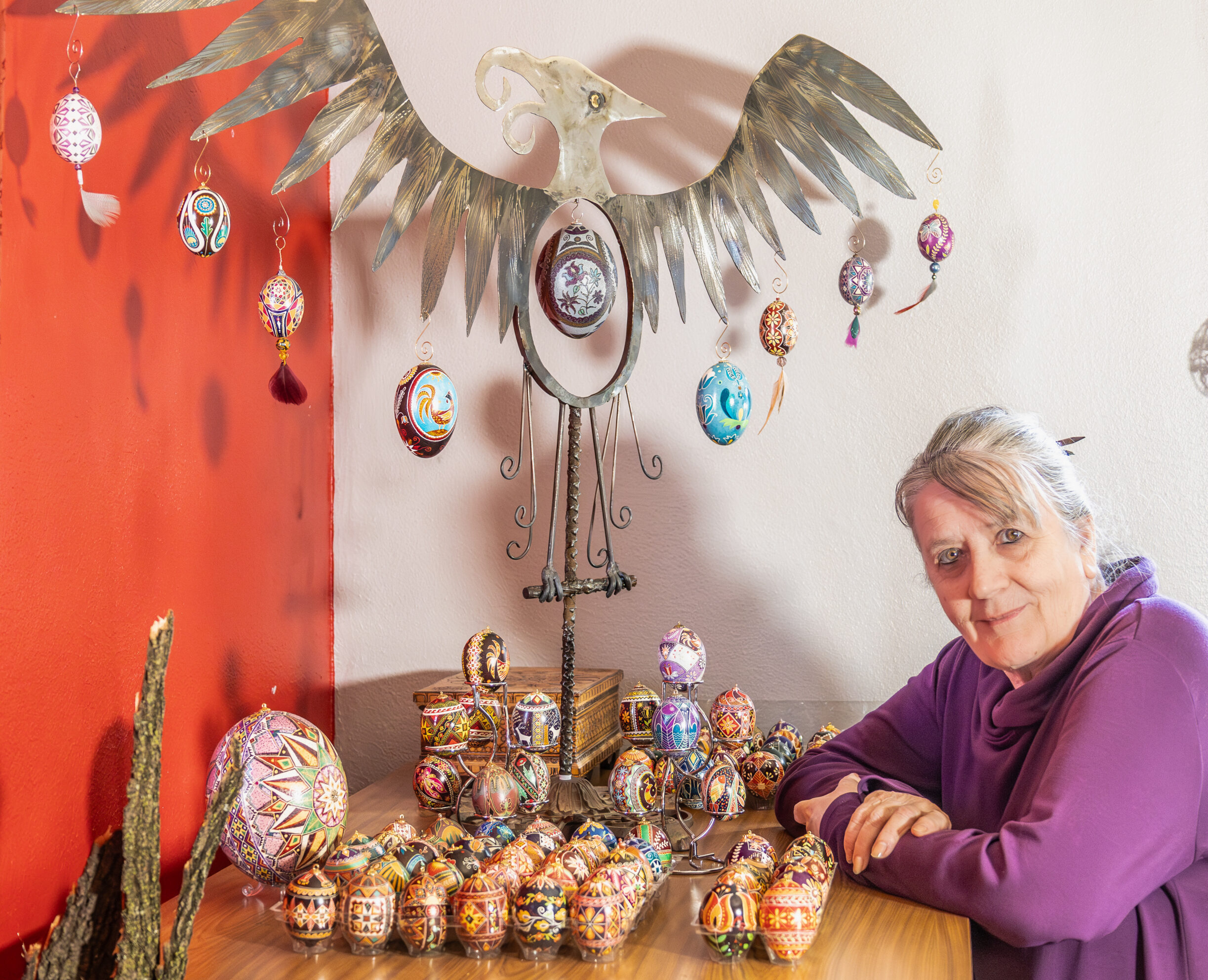 A person with light skin tone and greying hair standing by a dresser with a bunch of decorative, wax-resist patterned eggs.
