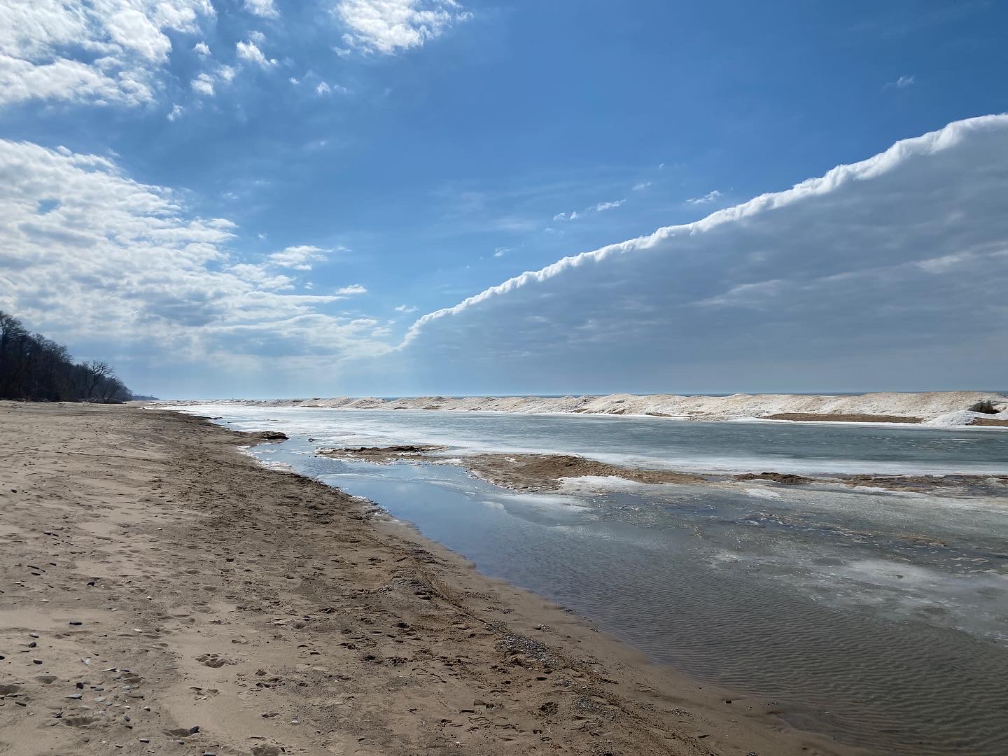 A sandy shoreline by a lake, with blue skies.