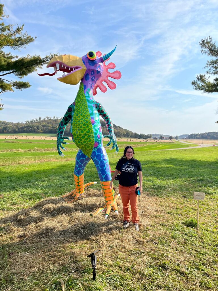 A person standing next to a tall colorful paper figure of a fantastical creature