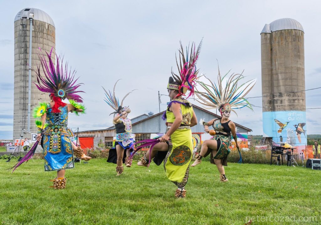 A group of performers dancing outdoors on farmland wearing traditional clothing and headgear.
