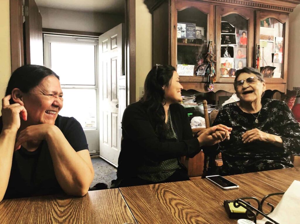 Three people with medium skin tones laugh at a table next to recording equipment.