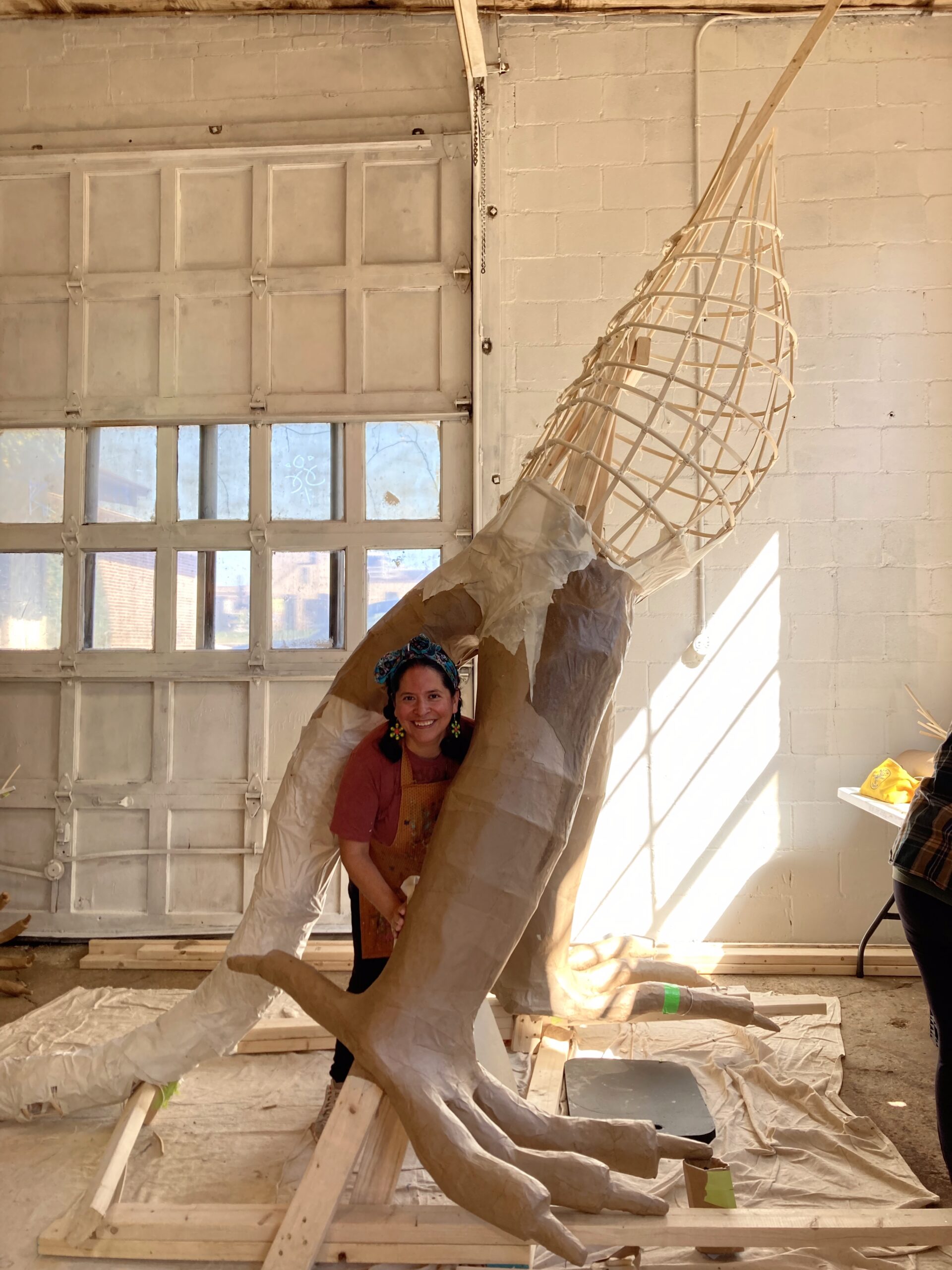 A person posing next to a large in-process sculptural work