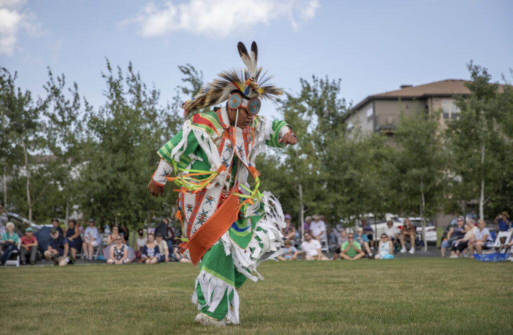 Bear Clan members dancing and singing as people watch in the background.