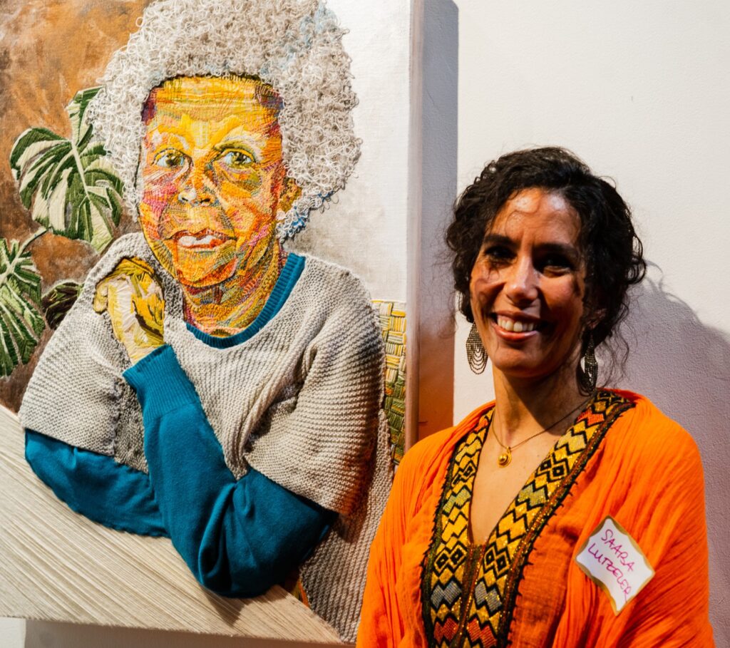 Artist Saaba Lutzeler smiles and poses next to one of her artworks.