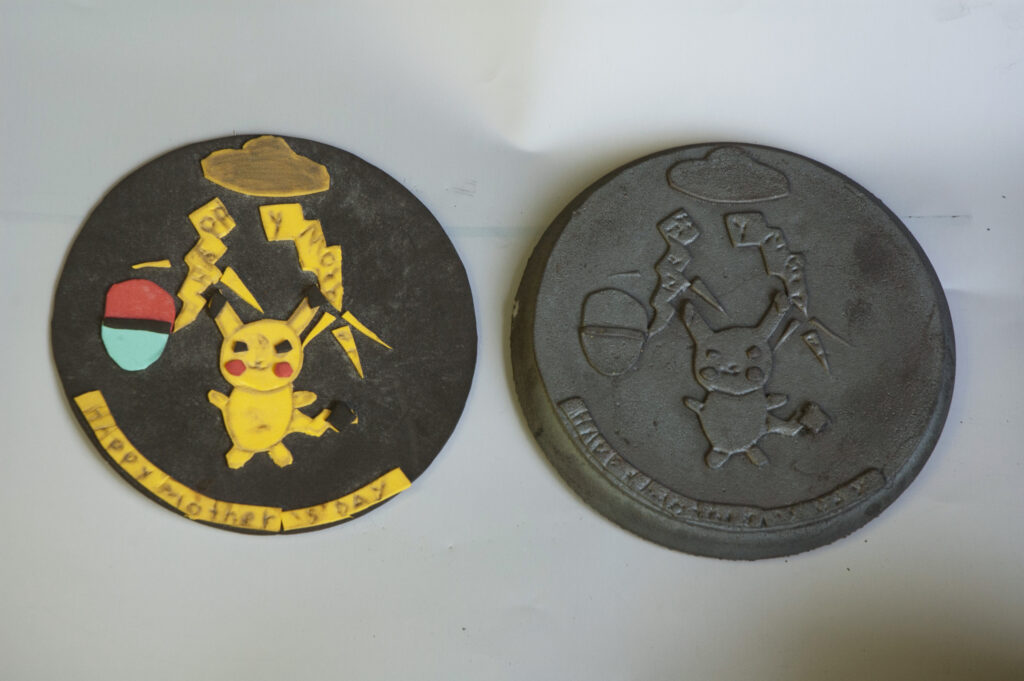 Two round artwork pieces depicting a cartoon character. They are almost identical with one made with foam cut outs and the other being a metal replication.