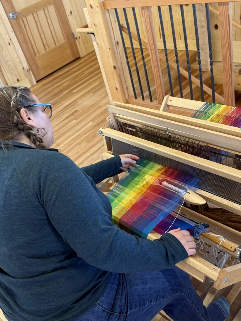 A woman with light skin works at a loom.