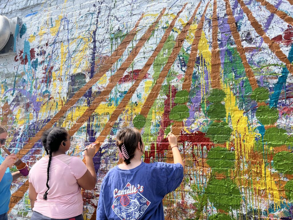 Two students paint art on a wall outdoors