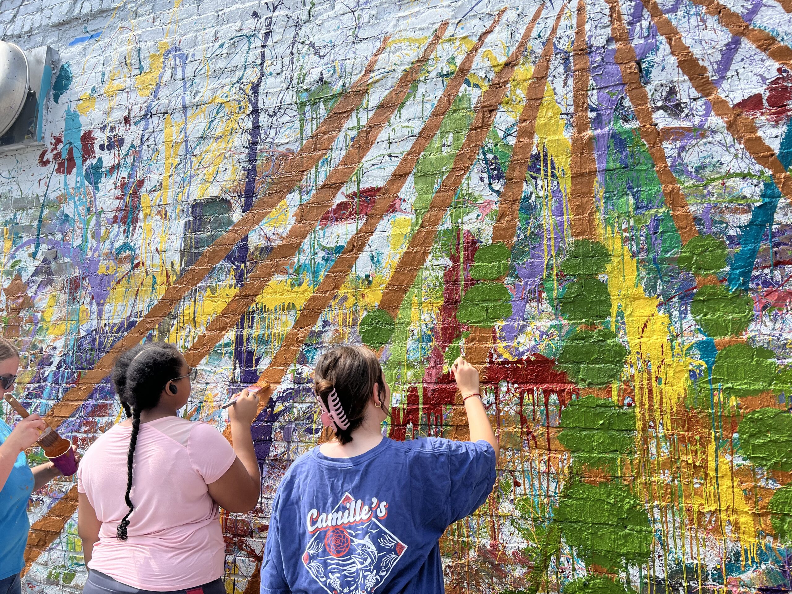 Two students paint art on a wall outdoors