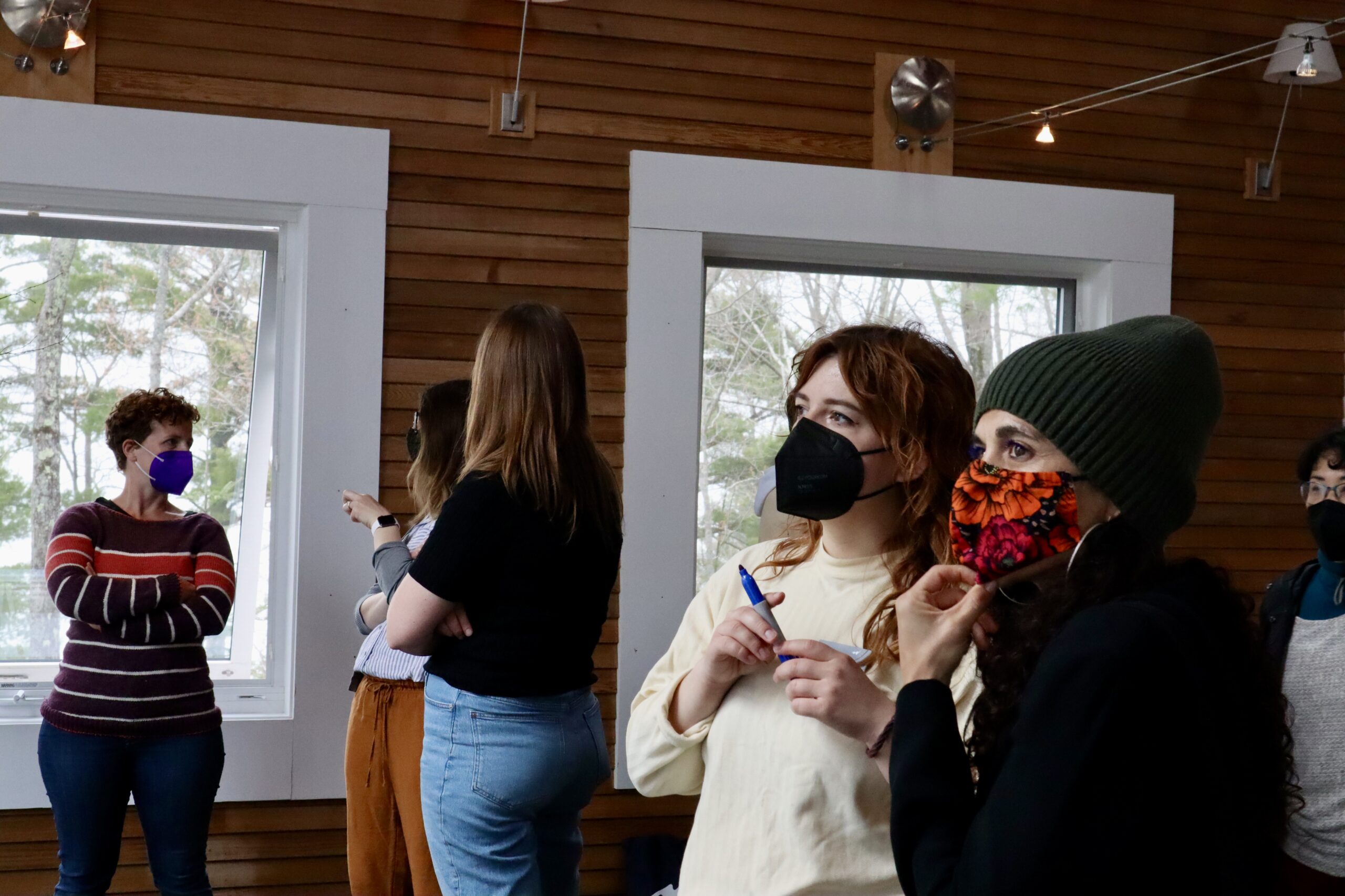 Two people in masks hold markers and look to the left.