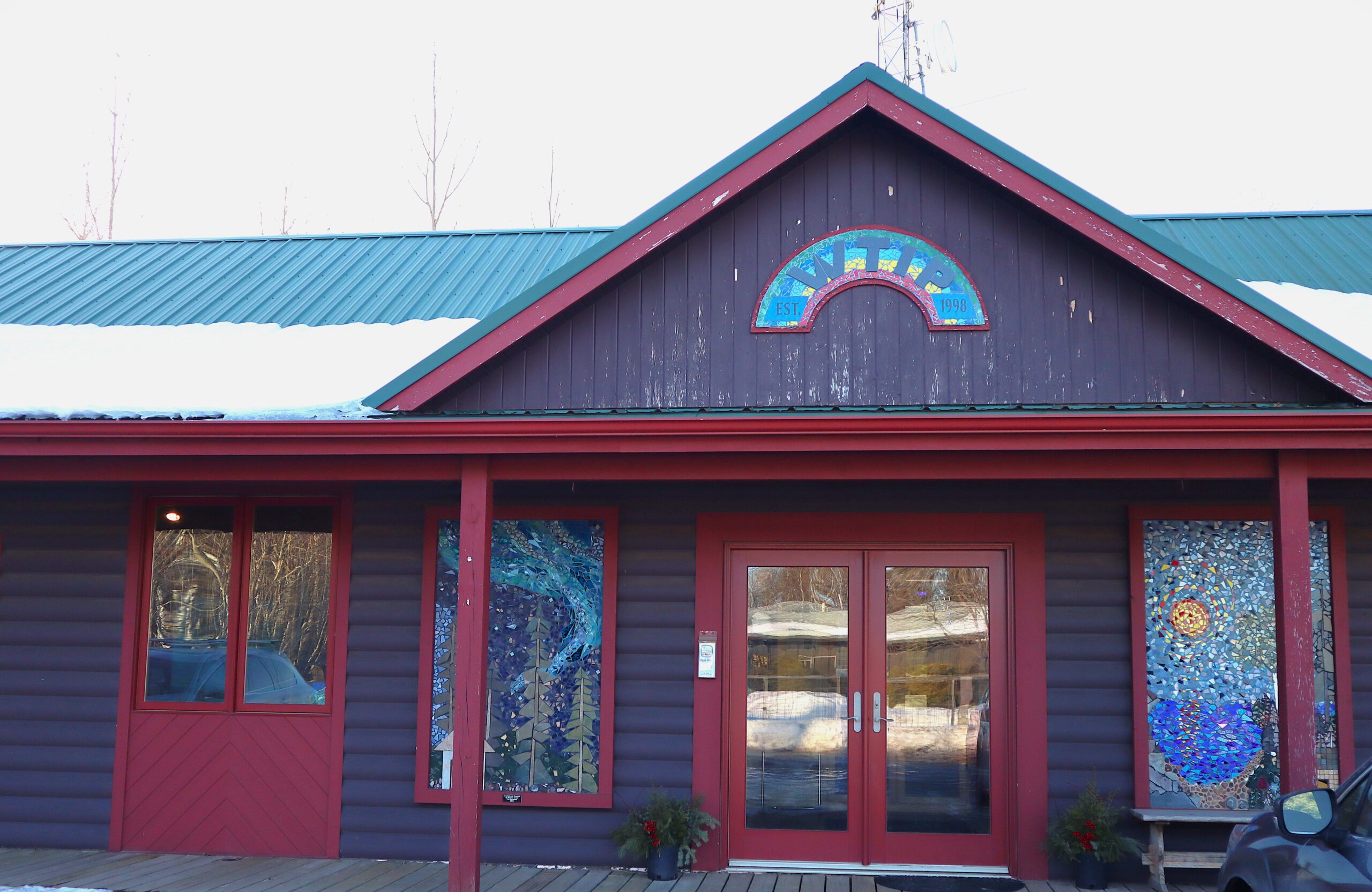 An exterior of a building with red trim and a green roof, complete with two large artworks.