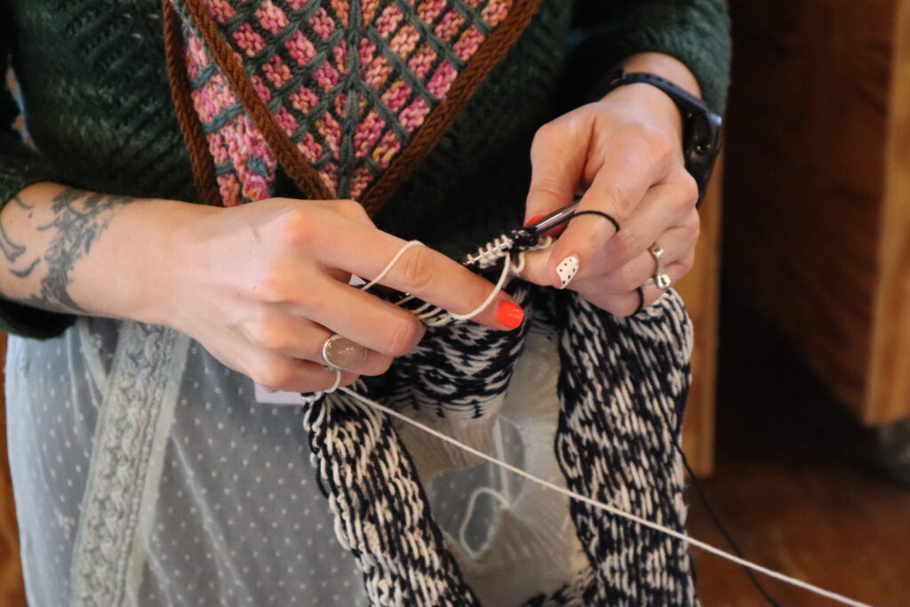 Light skinned hands with painted nails creating a needle and yarn craft.