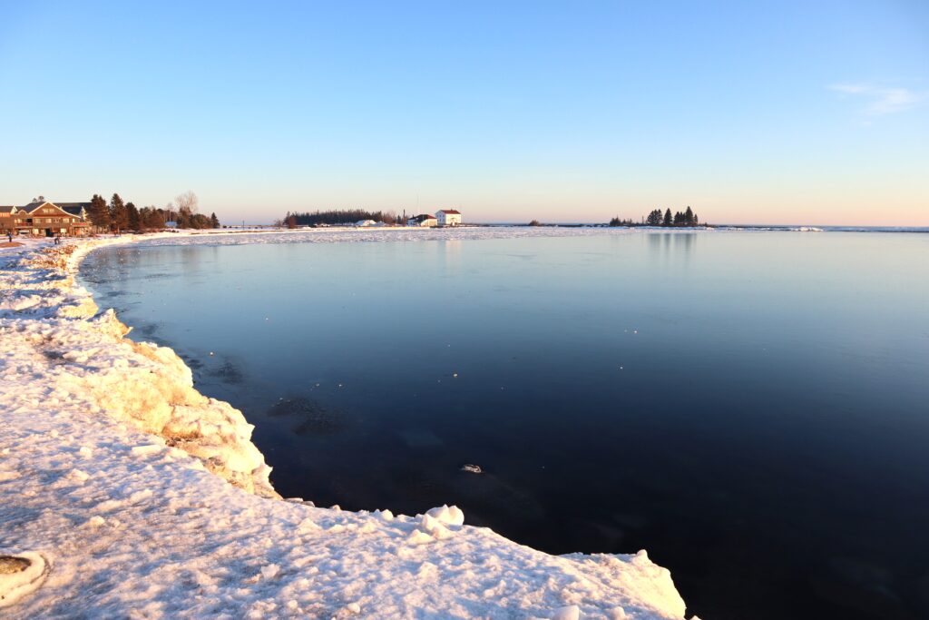 A winter shoreline of still blue waters and snow.