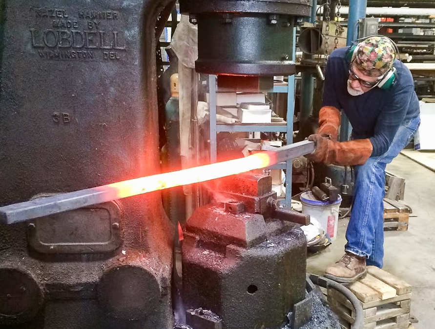 A person holding a long, hot and glowing metal pole as they shape it with a large machine.