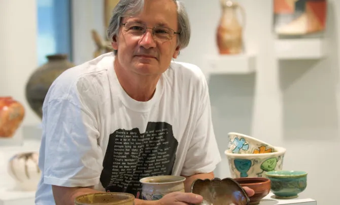 A man with light skin holds a bowl and is surrounded by several bowls.