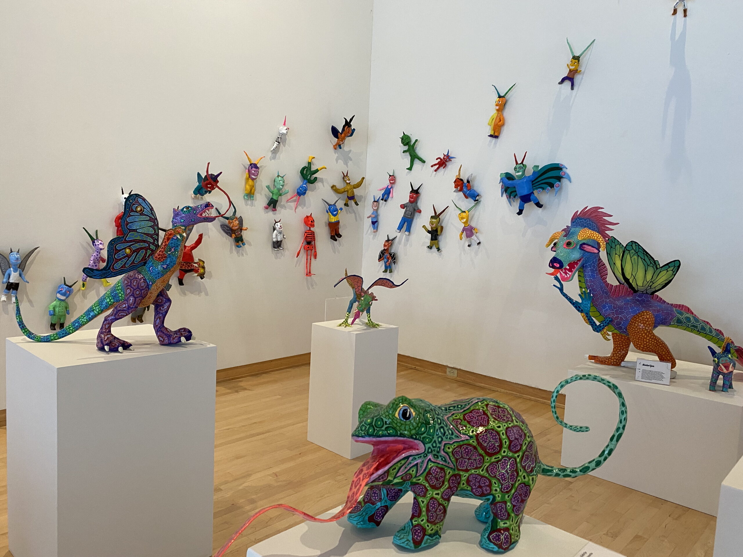 Colorful fantastical painted sculptural paper figures on display on pedestals and mounted on a white wall