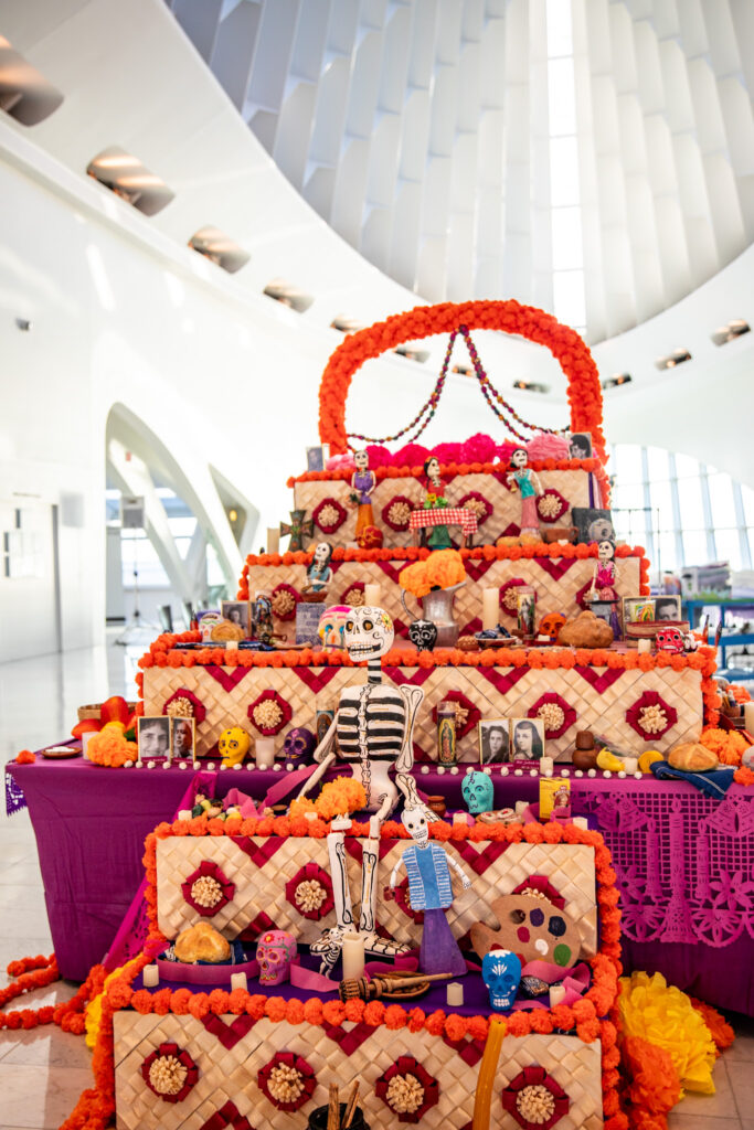 A Mexican altar or ofrenda decorated with bright orange marigold flowers, photos and other sculptures.