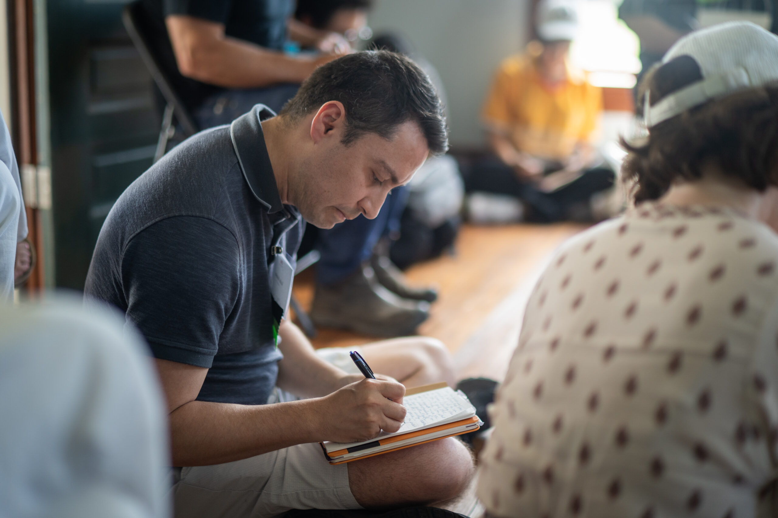 Man seated on the floor writing in a notebook during a group workshop.