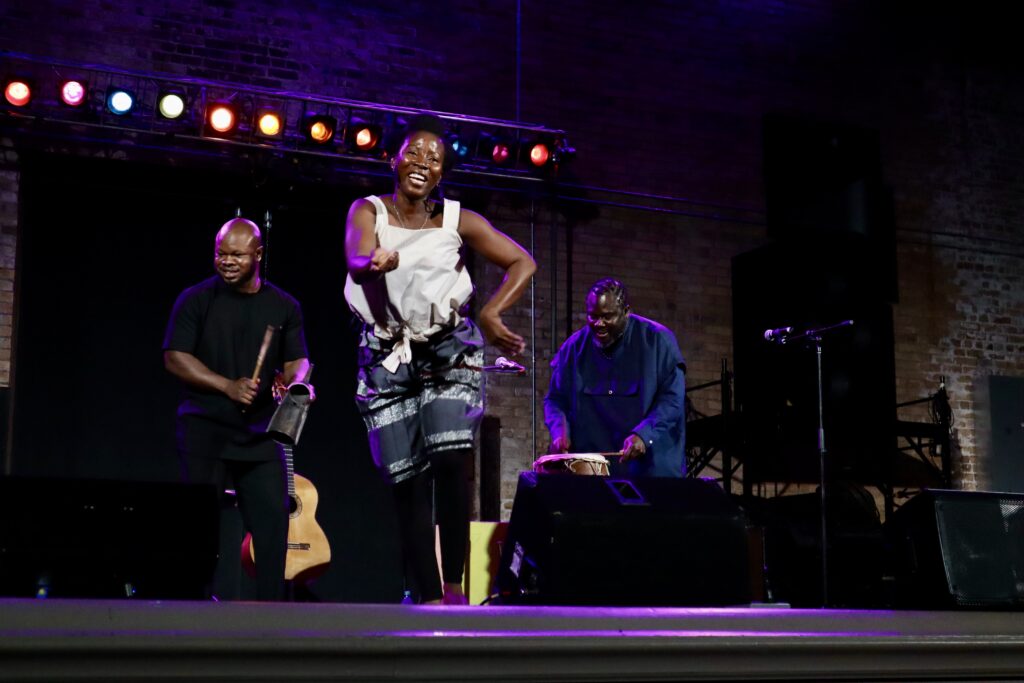 A woman dances on stage surrounded by two Ghanaian musicans.