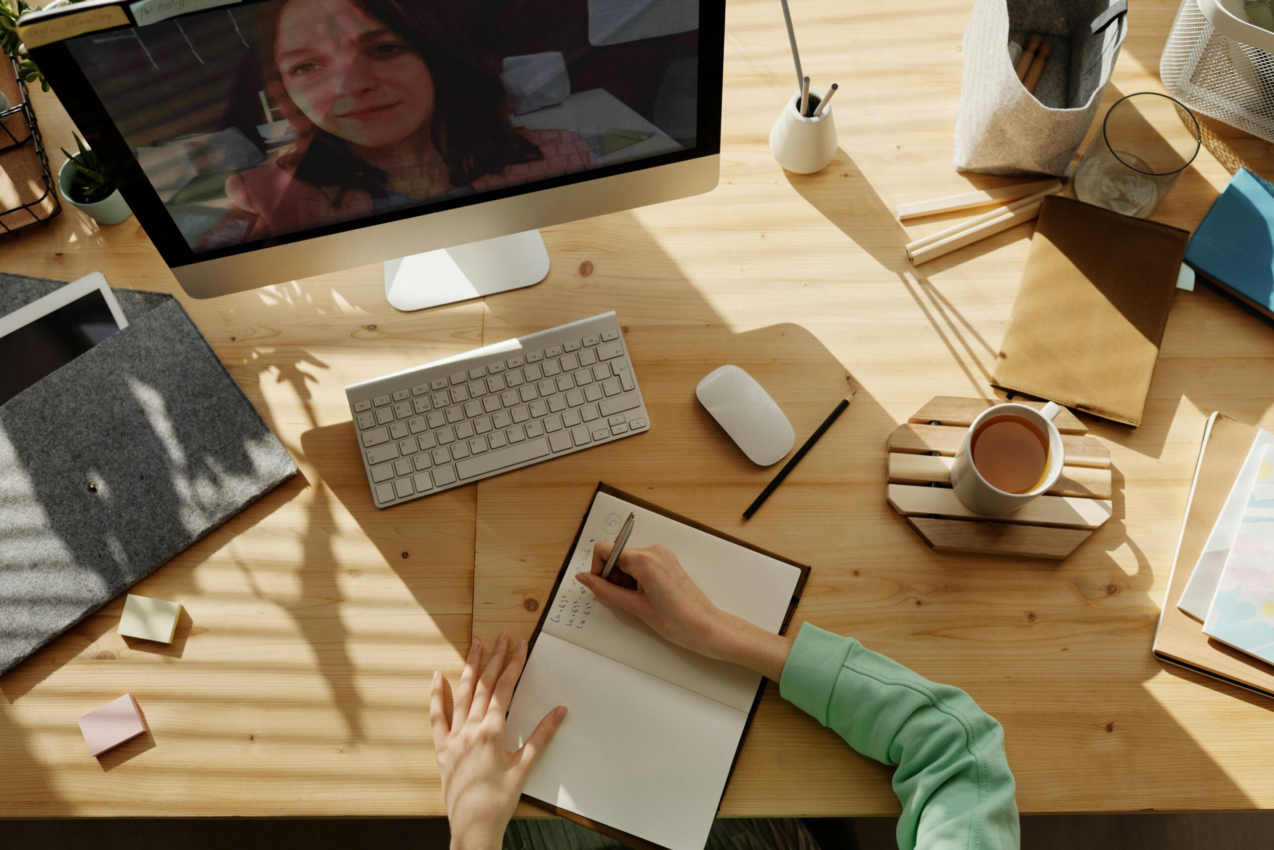 A person with light skin writes in a journal while being on Zoom with another person