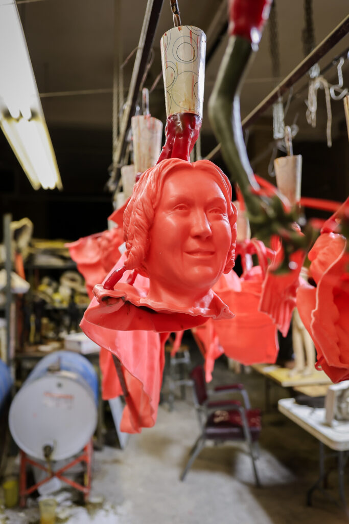 Bright red wax molds of women’s heads hang from hooks in a sculpture studio, part of the bronze casting process for the Ohio Women’s Monument.