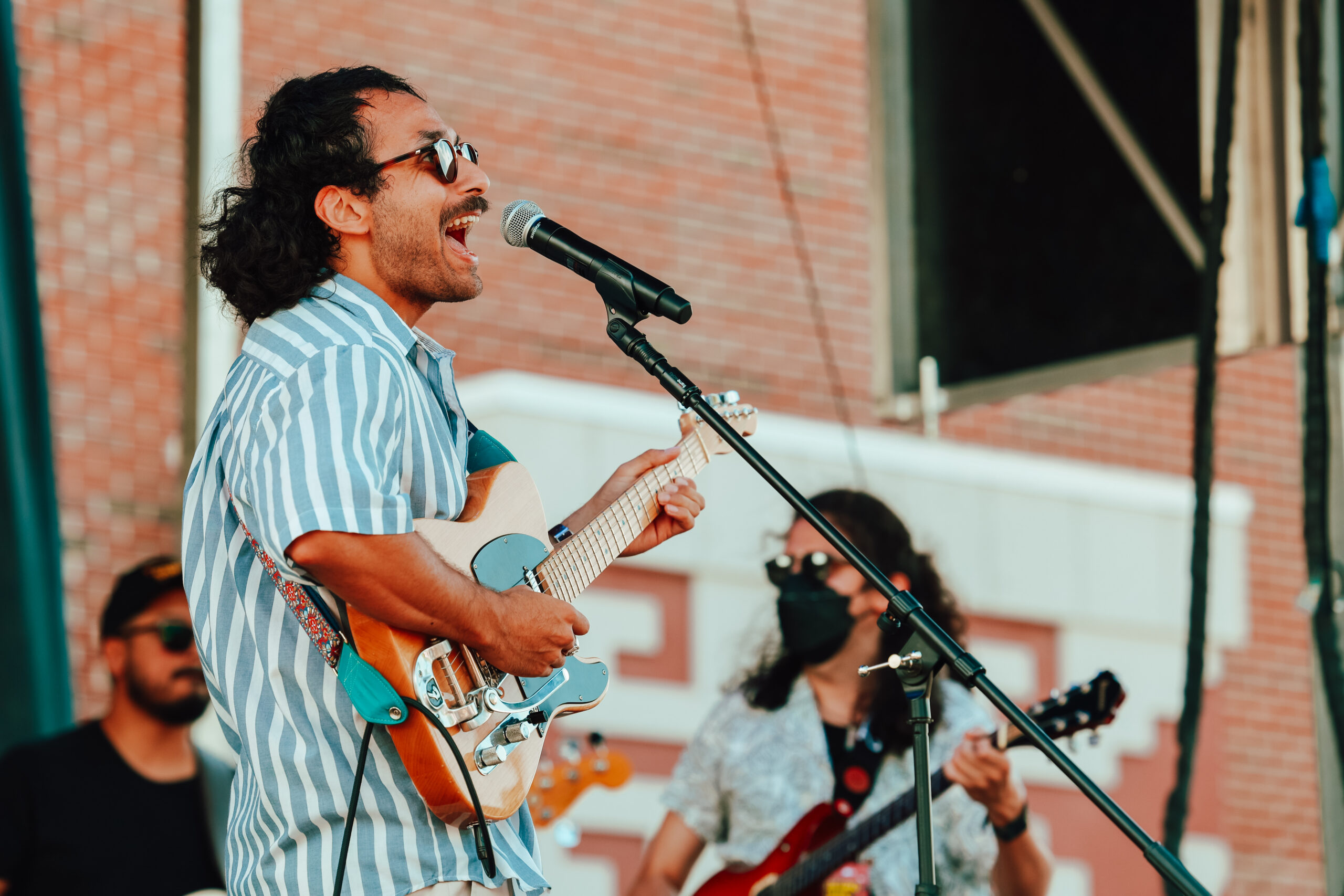 A person of medium skin tone signing into a microphone. They are playing an electric guitar.