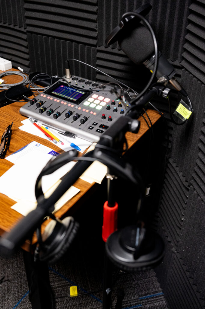 A corner of a room with audio recording equipment including a mixing board, microphone, and headphones.