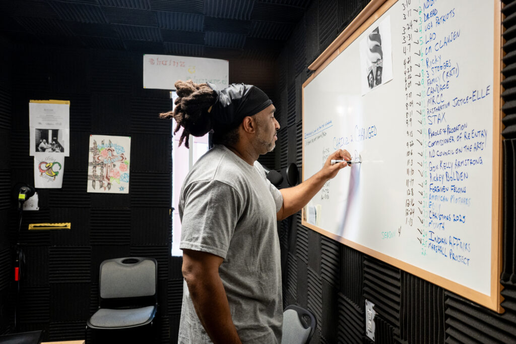 A person standing next to a whiteboard holding a marker and writing on it.