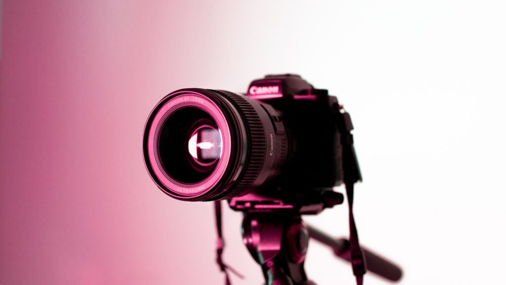 A black DSLR camera points left into a pink light
