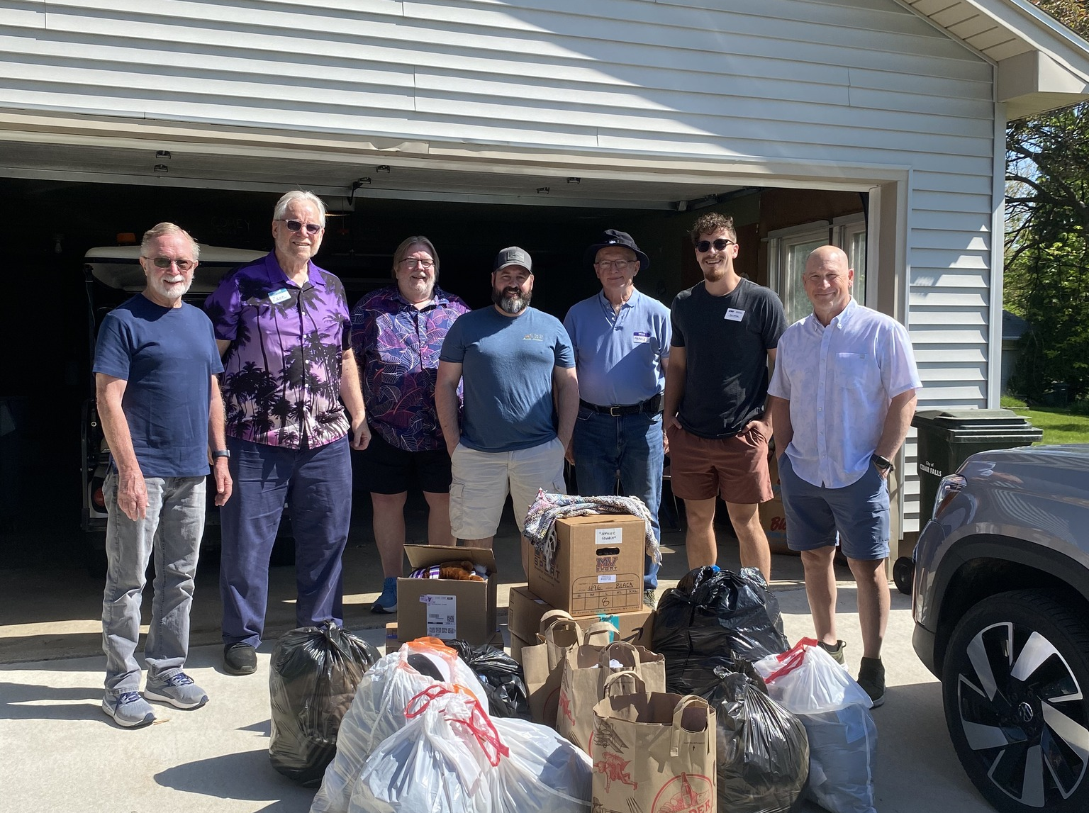 Seven men standing in front of an open garage with bags.