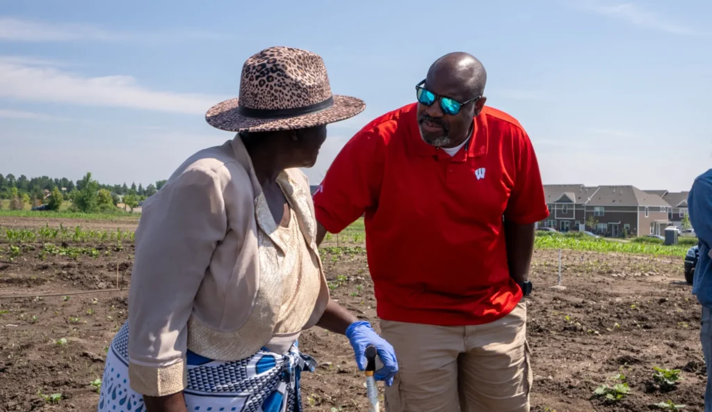 Two people in a field that is mostly dirt. One puts their hand on the others back and looks at them.
